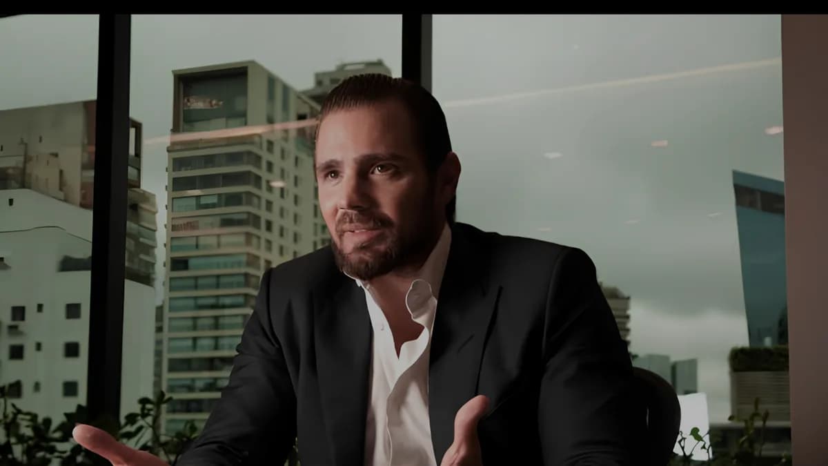 Homem sentado à mesa em um escritório, diante de uma grande janela com vista para edifícios urbanos, gesticulando enquanto fala. A imagem transmite uma conversa profissional e reflexiva, relacionada à atuação jurídica e à análise de estratégias no contexto criminal.