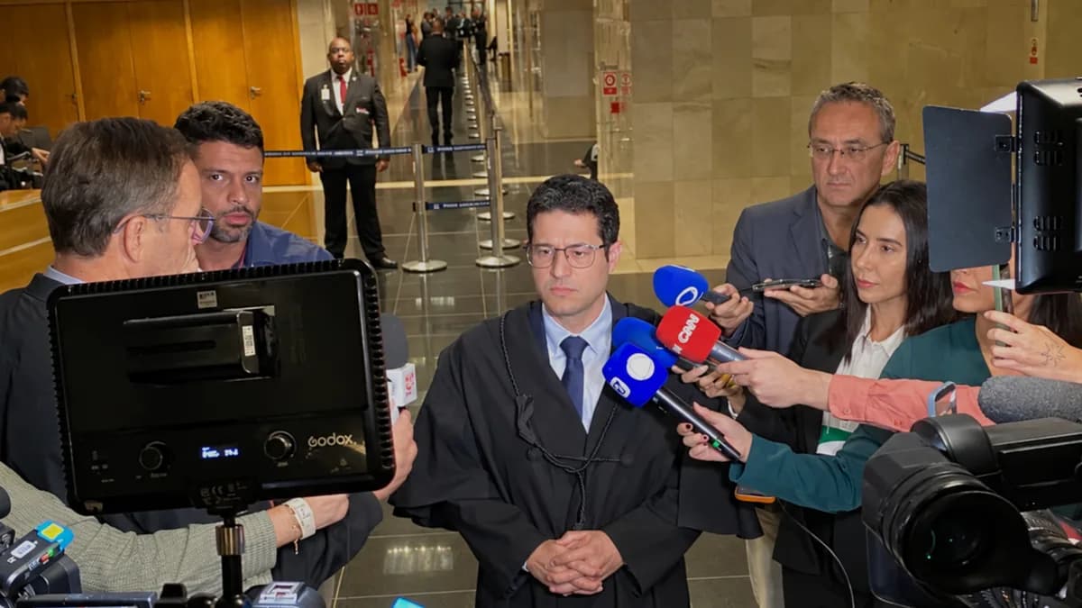 Foto de um advogado cercado por jornalistas e câmeras durante entrevista em um tribunal.