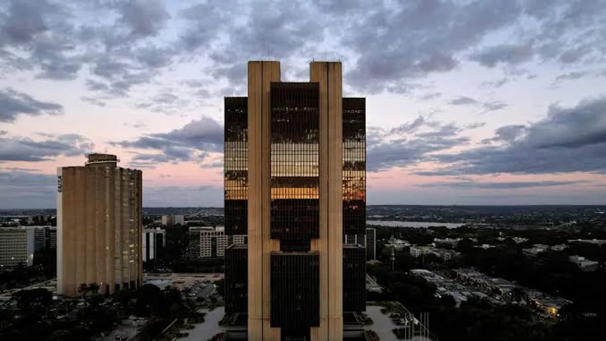 Vista aérea de Brasília ao entardecer, com destaque para o edifício do Banco Central do Brasil ao centro e o horizonte da cidade ao fundo.