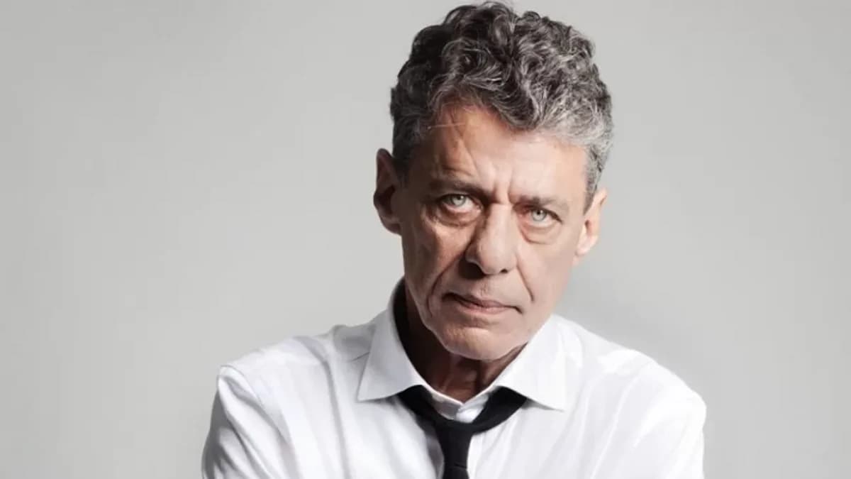 Chico Buarque, de cabelos grisalhos, veste camisa branca e gravata preta e olha diretamente para a câmera, em retrato sobre fundo cinza claro.