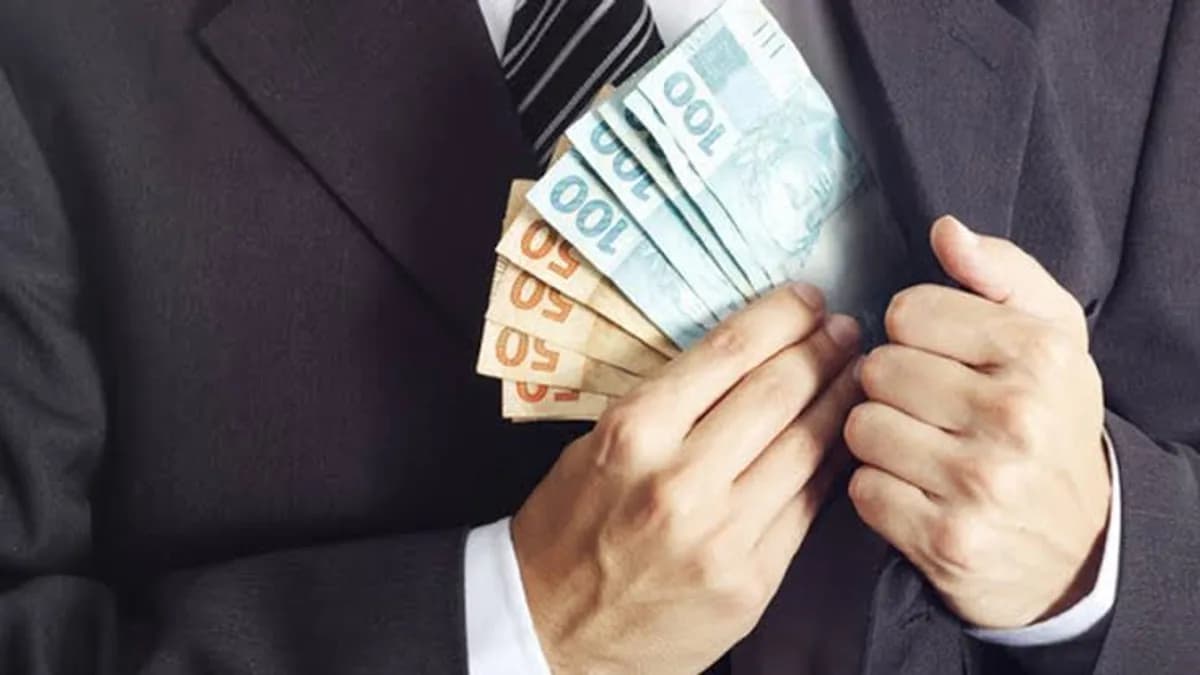 Homem de terno segurando e escondendo cédulas de dinheiro junto ao peito, representando visualmente a ocultação de valores e práticas relacionadas à lavagem de dinheiro.