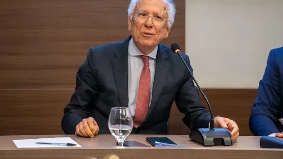 Nabor Bulhões, advogado, durante conferência acadêmica, sentado à mesa de exposição, usando terno escuro e gravata vermelha, com microfone à sua frente.